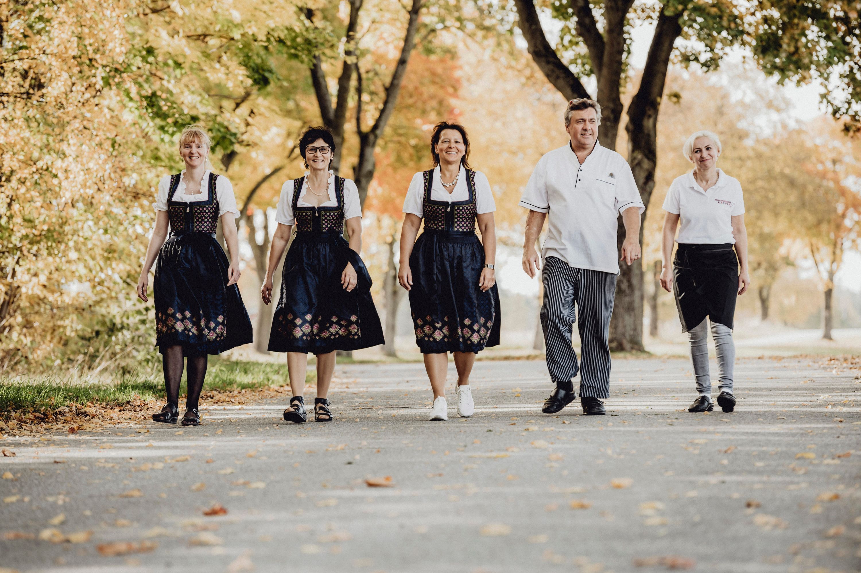 Fünf Personen in traditioneller Kleidung gehen auf einer von Bäumen gesäumten Straße.