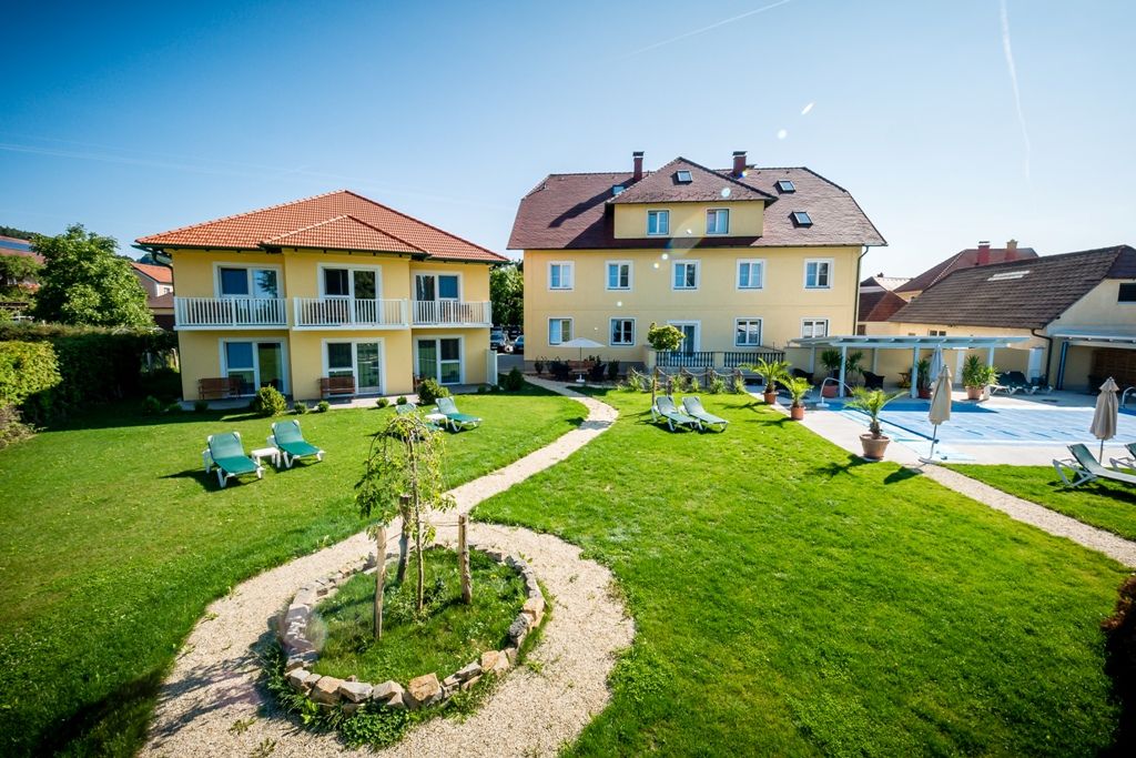 Garden area with yellow buildings and sun loungers in sunny weather.