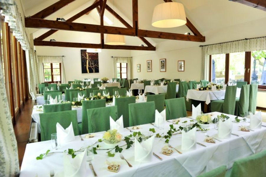 Innenansicht eines festlich gedeckten Gasthauses mit grünen Stühlen und Holzbalken.