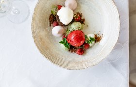 Ein Dessert mit verschiedenen Eiskugeln, Himbeeren und Minzbl&auml;ttern auf einem Teller.