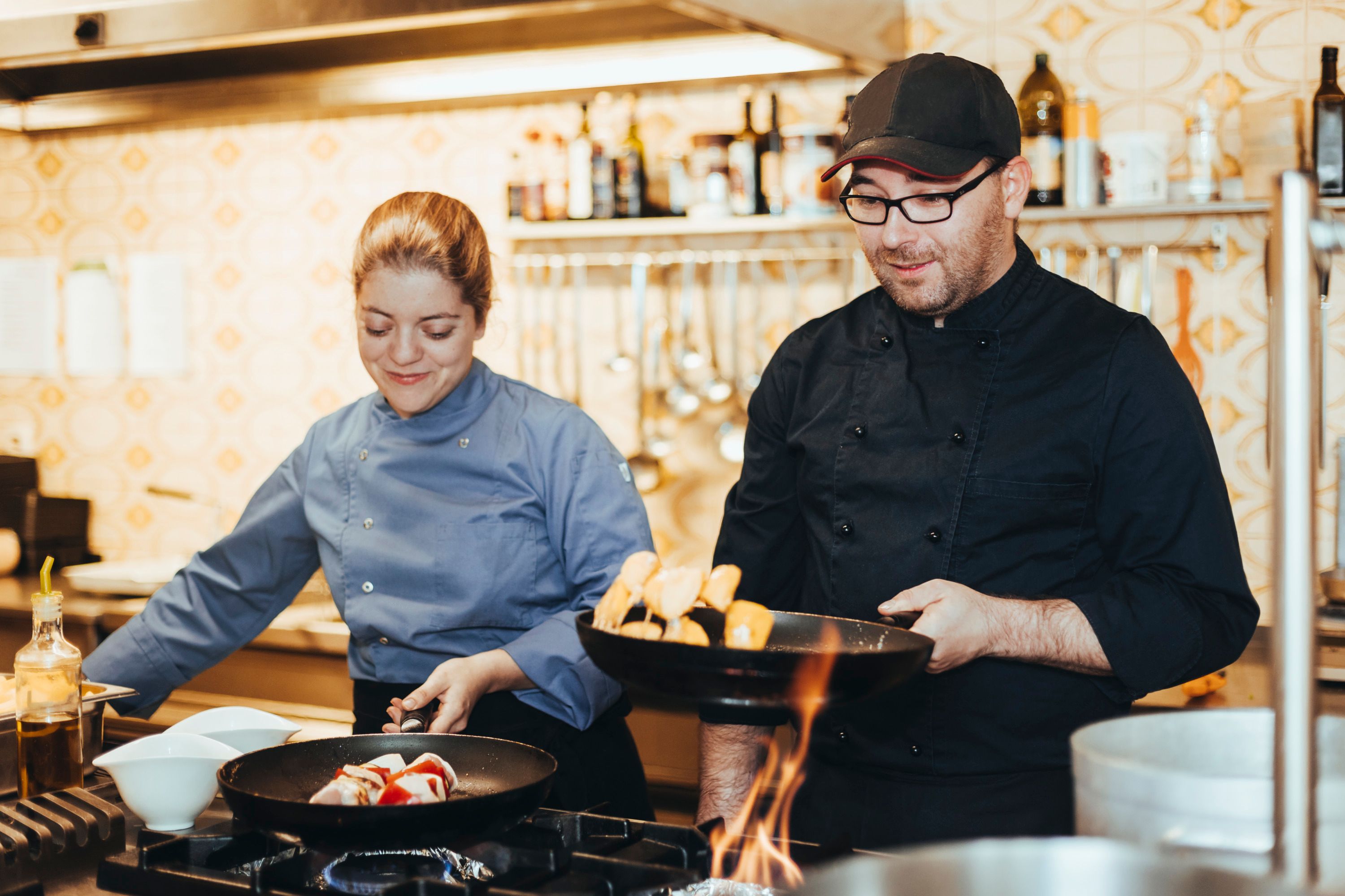 Two chefs in a kitchen working at a stove.