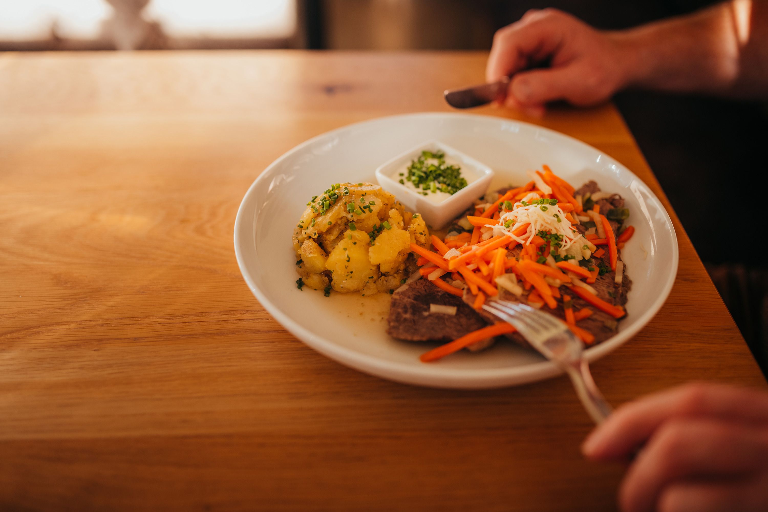 Teller mit Fleisch, Karotten, Kartoffeln und Dip auf Holztisch.