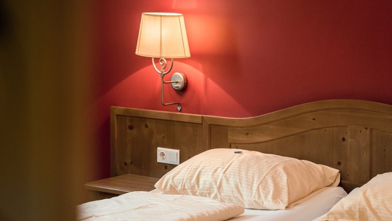 Ein gemütliches Doppelzimmer mit Holzkopfteil, roter Wand und Wandlampe.