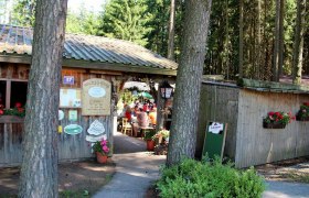 Eingang zu einer Waldschenke mit Holzhütte und Blumen.