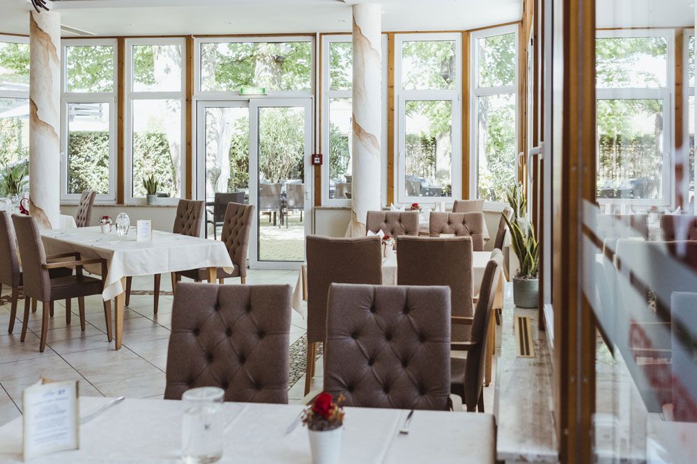 Innenansicht eines eleganten Restaurants mit gedeckten Tischen und großen Fenstern.