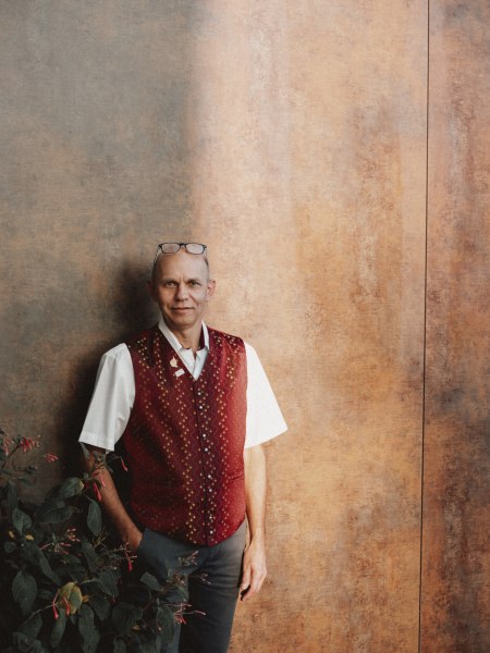 Ein Mann in traditioneller Weste lehnt an einer Wand.
