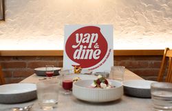 Gedeckter Tisch mit verschiedenen Gerichten und Getränken bei „yap&dine“. Im Hintergrund steht ein Schild mit dem „yap&dine“-Logo und dem Text "Das Wirtshaus ist zum Teilen da.".