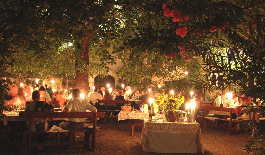 Abendessen im Freien unter einem Baum mit Kerzenlicht und vielen G&auml;sten.