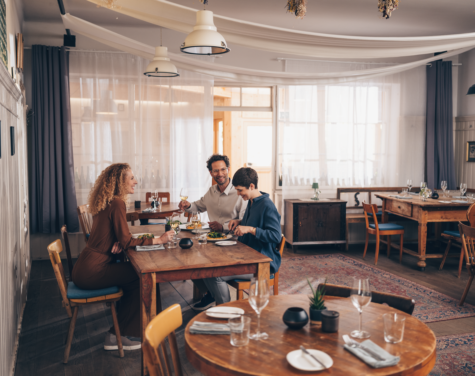 In einem einladenden Wirtshaus genießen eine Familie und ein Kind ein köstliches Mahl, umgeben von rustikalem Holzinterieur und sanften Lichtakzenten. Die Atmosphäre ist warm und freundlich, ideal für gesellige Stunden und kulinarische Entdeckungen in der Region. Hier wird die Wirtshauskultur Niederösterreichs lebendig.