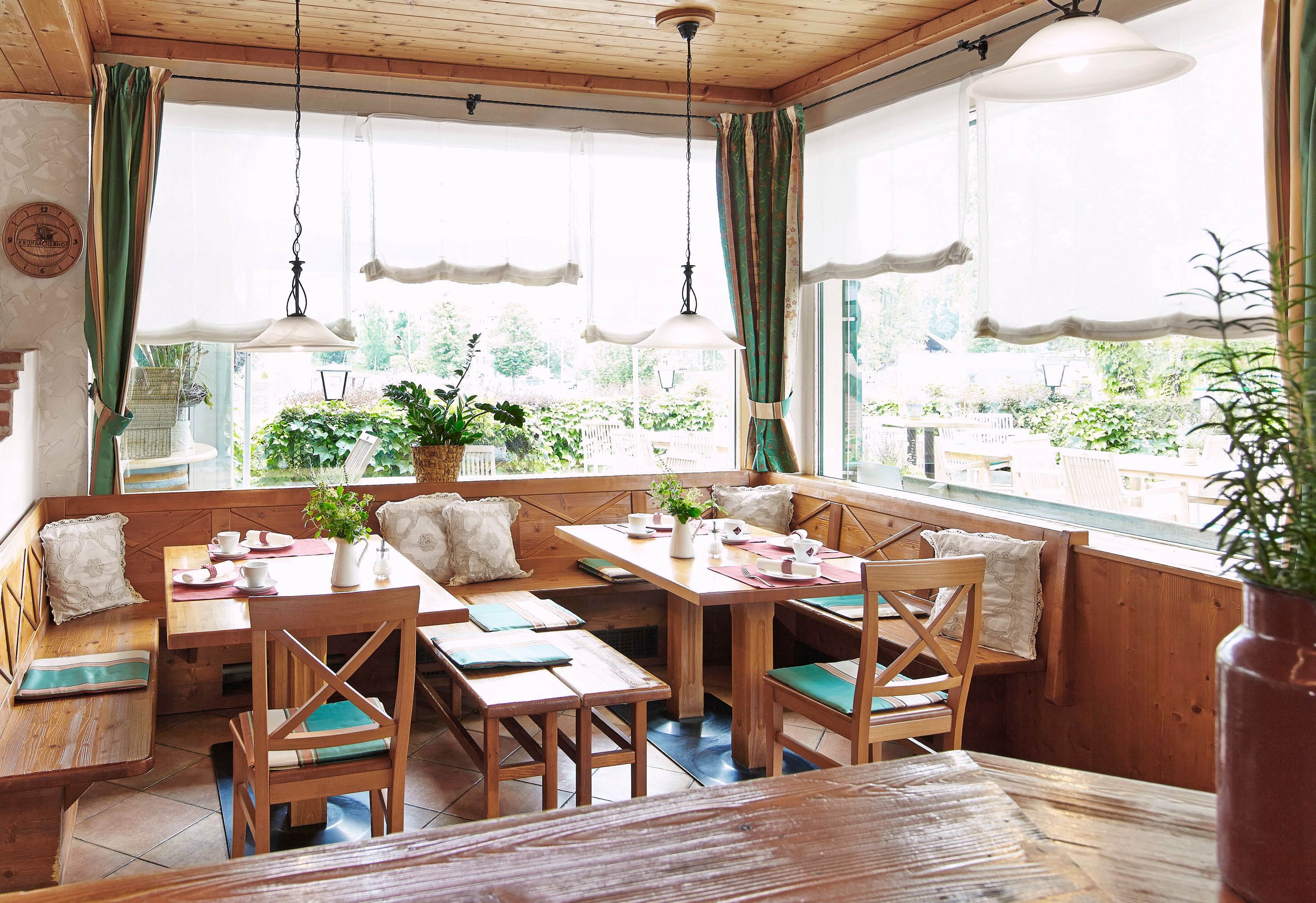 Gemütlicher Frühstücksraum mit Holzmöbeln und großen Fenstern, die auf eine Terrasse blicken.