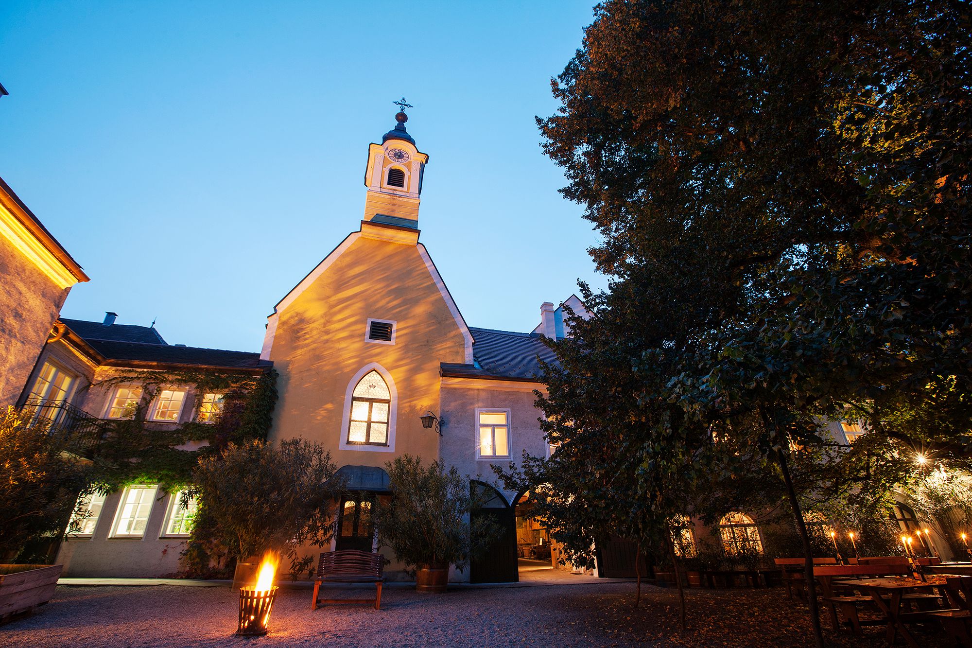 Ein beleuchtetes historisches Gebäude mit einem kleinen Turm und einem Innenhof bei Dämmerung.