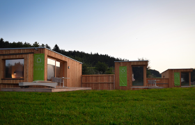 Moderne Holzh&uuml;tten auf einer Wiese bei Sonnenuntergang.