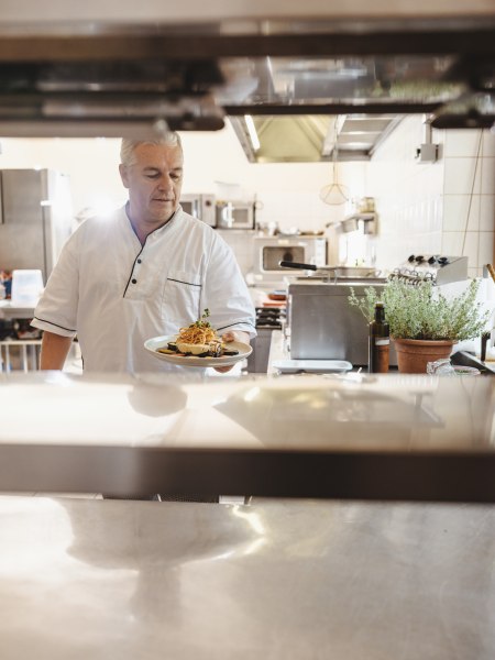 Ein Koch in einer Restaurantk&uuml;che h&auml;lt einen Teller mit Essen in der Hand.