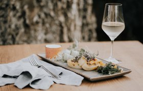 Kartoffelroulade mit Kürbis und Schafkäse auf einem Teller, daneben ein Glas Weißwein.