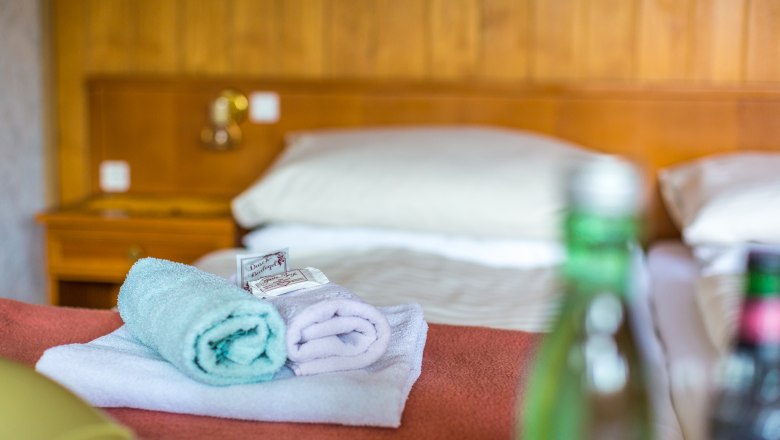 Hotelzimmer mit Bett, Handt&uuml;chern und Wasserflaschen.