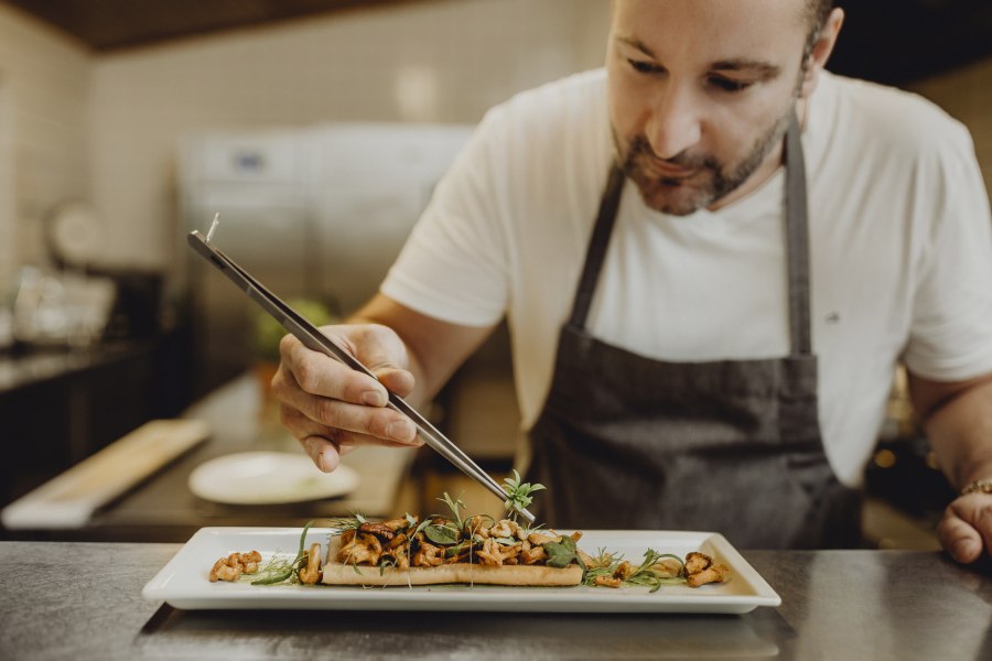 Ein Koch richtet ein Gericht mit einer Pinzette auf einem Teller an.