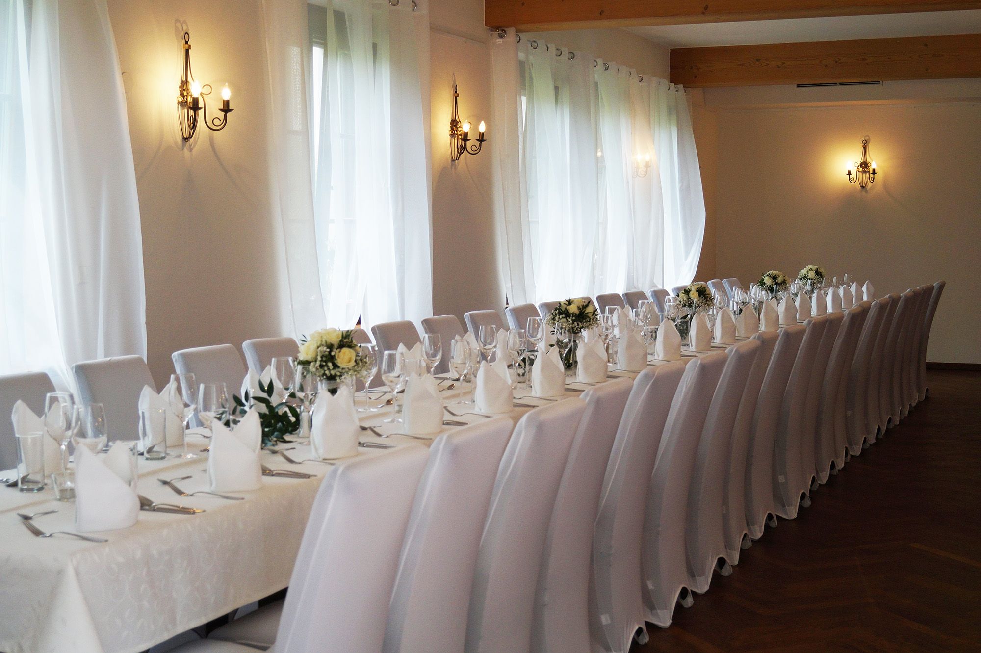 Eleganter Veranstaltungssaal mit langen, festlich gedeckten Tischen und weißen Stühlen.