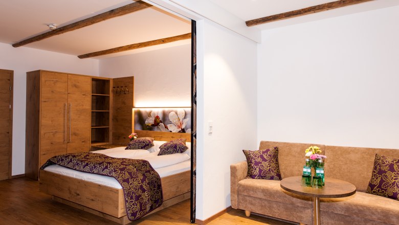 Gem&uuml;tliches Hotelzimmer mit Holzm&ouml;beln, Doppelbett, Sofa und kleinem Tisch.