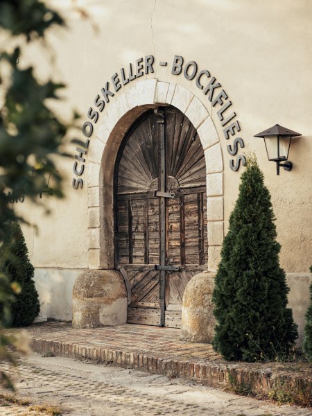 Eingang zum Schlosskeller mit Holztür und Schriftzug 'Schlosskeller - Bockfließ'.
