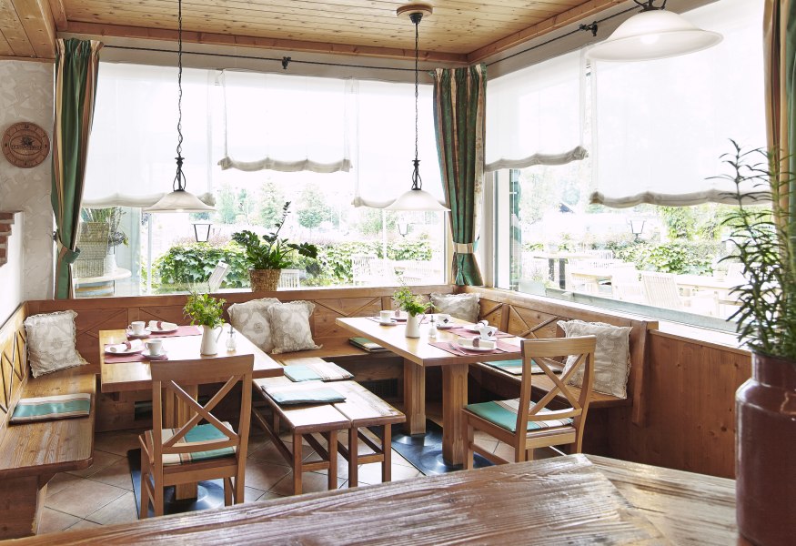 Gemütlicher Frühstücksraum mit Holzmöbeln und großen Fenstern, die auf eine Terrasse blicken.