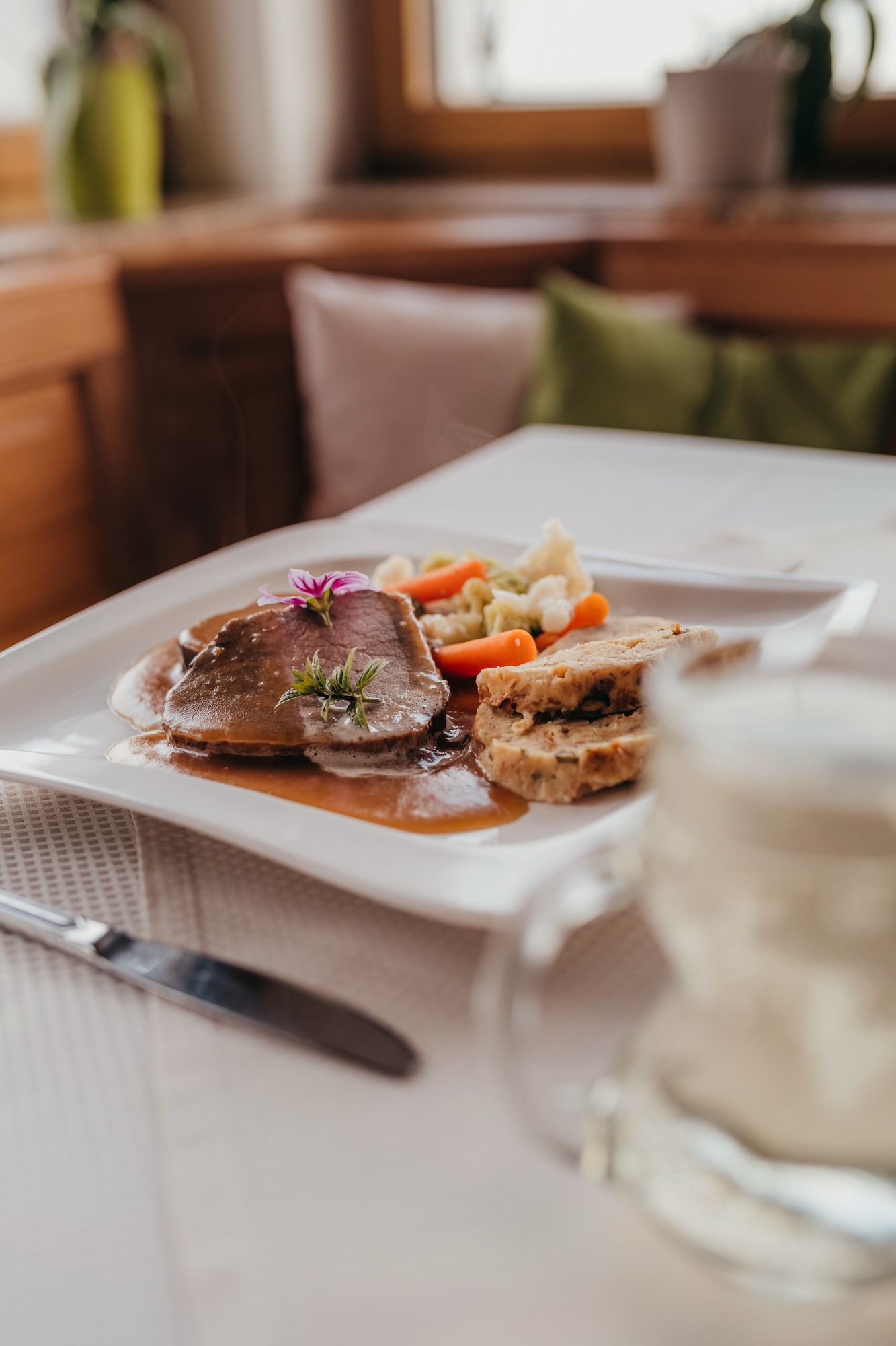 Ein Teller mit Mostbraten, Semmelknödel und Gemüse auf einem Tisch.