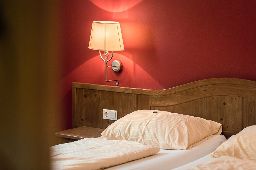 Ein gemütliches Doppelzimmer mit Holzkopfteil, roter Wand und Wandlampe.