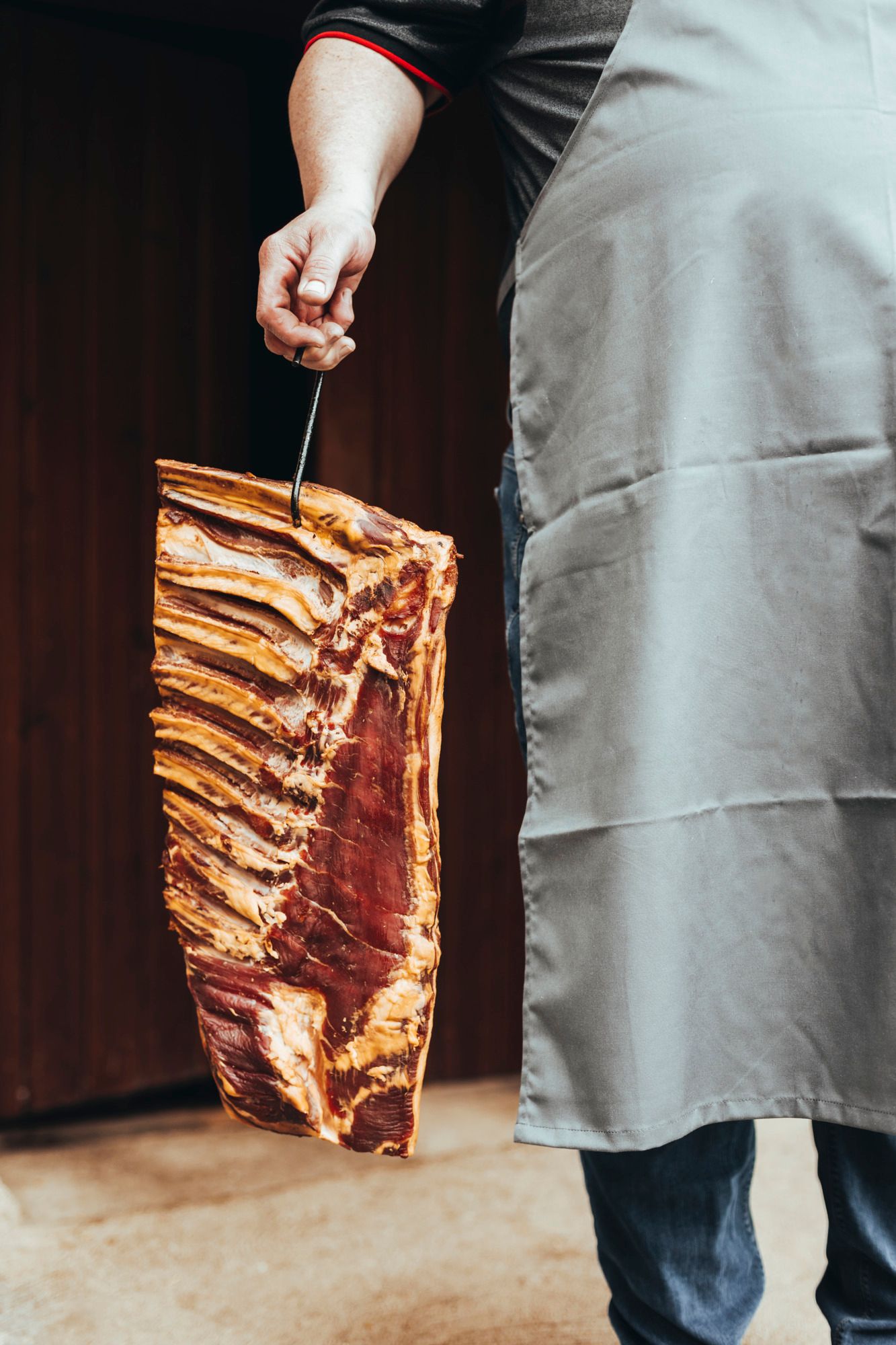 Person hält ein großes Stück Fleisch mit Rippen an einem Haken.