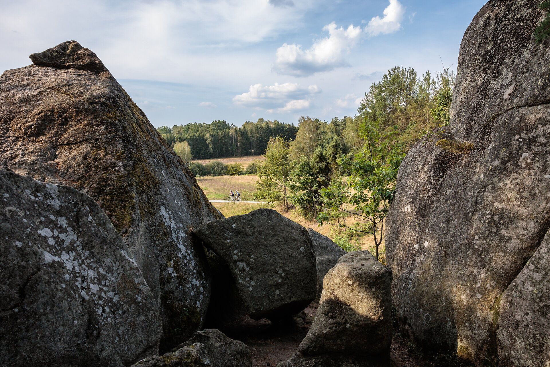 Zwischen majestätischen Felsen erstreckt sich eine malerische Landschaft, die zum Verweilen einlädt. Die sanften Hügel und das üppige Grün schaffen eine harmonische Kulisse, während die Wolken am Himmel für eine entspannte Atmosphäre sorgen.