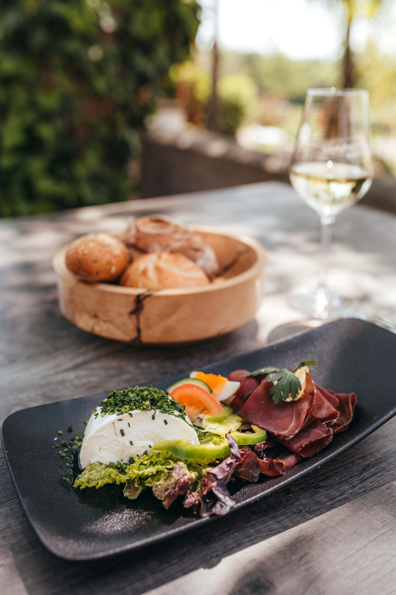 Schwarzer Teller mit Schafkäse, Schinken, Gemüse und Gebäck im Freien präsentiert.