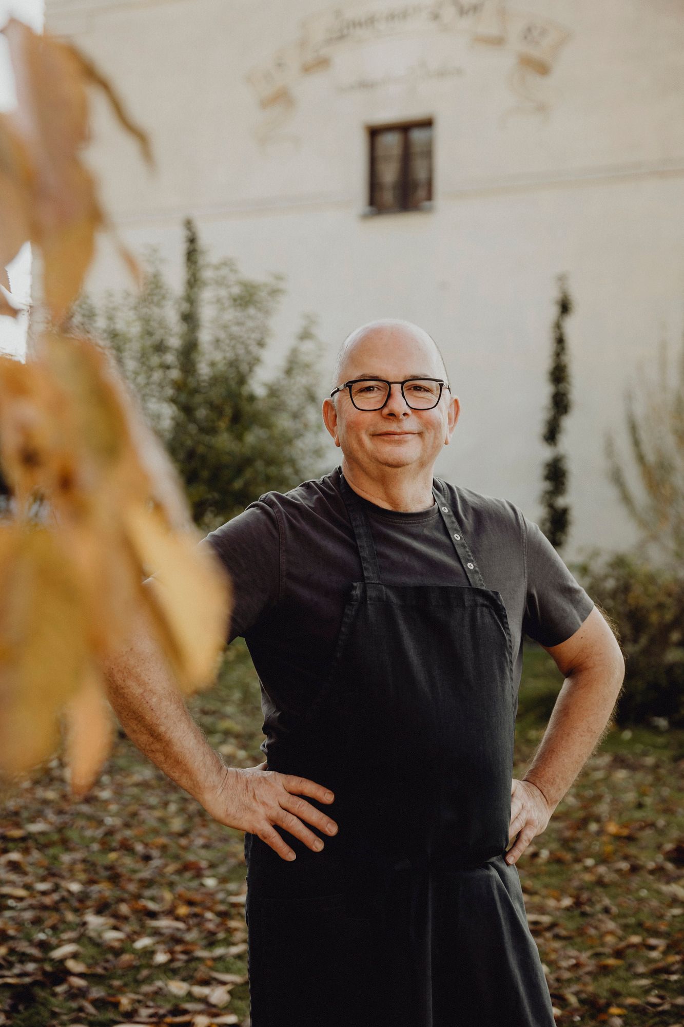 Mann mit Brille und Schürze steht lächelnd im herbstlichen Garten.