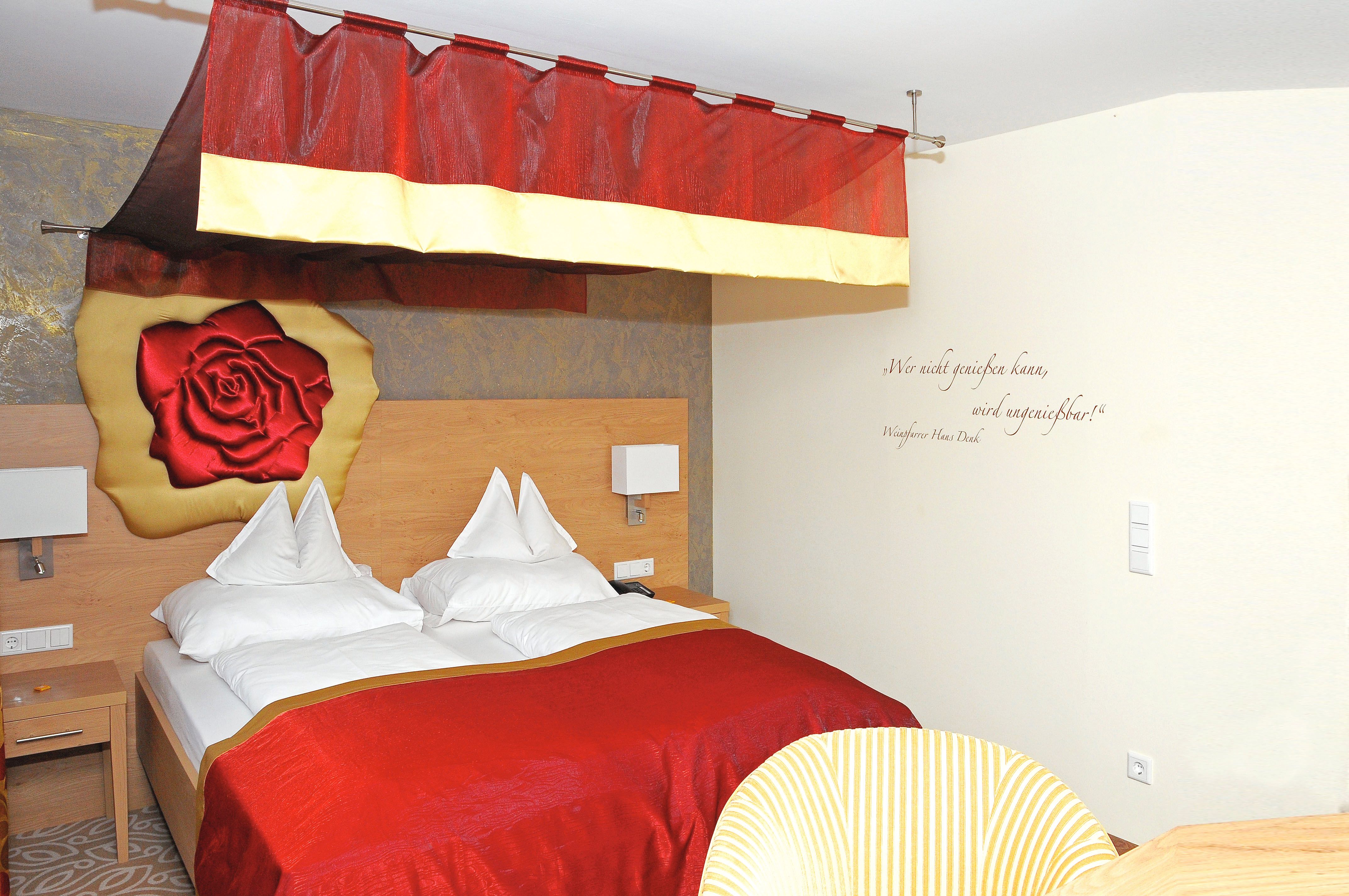 Gemütliches Hotelzimmer mit rotem Baldachin und Rosenmotiv an der Wand.