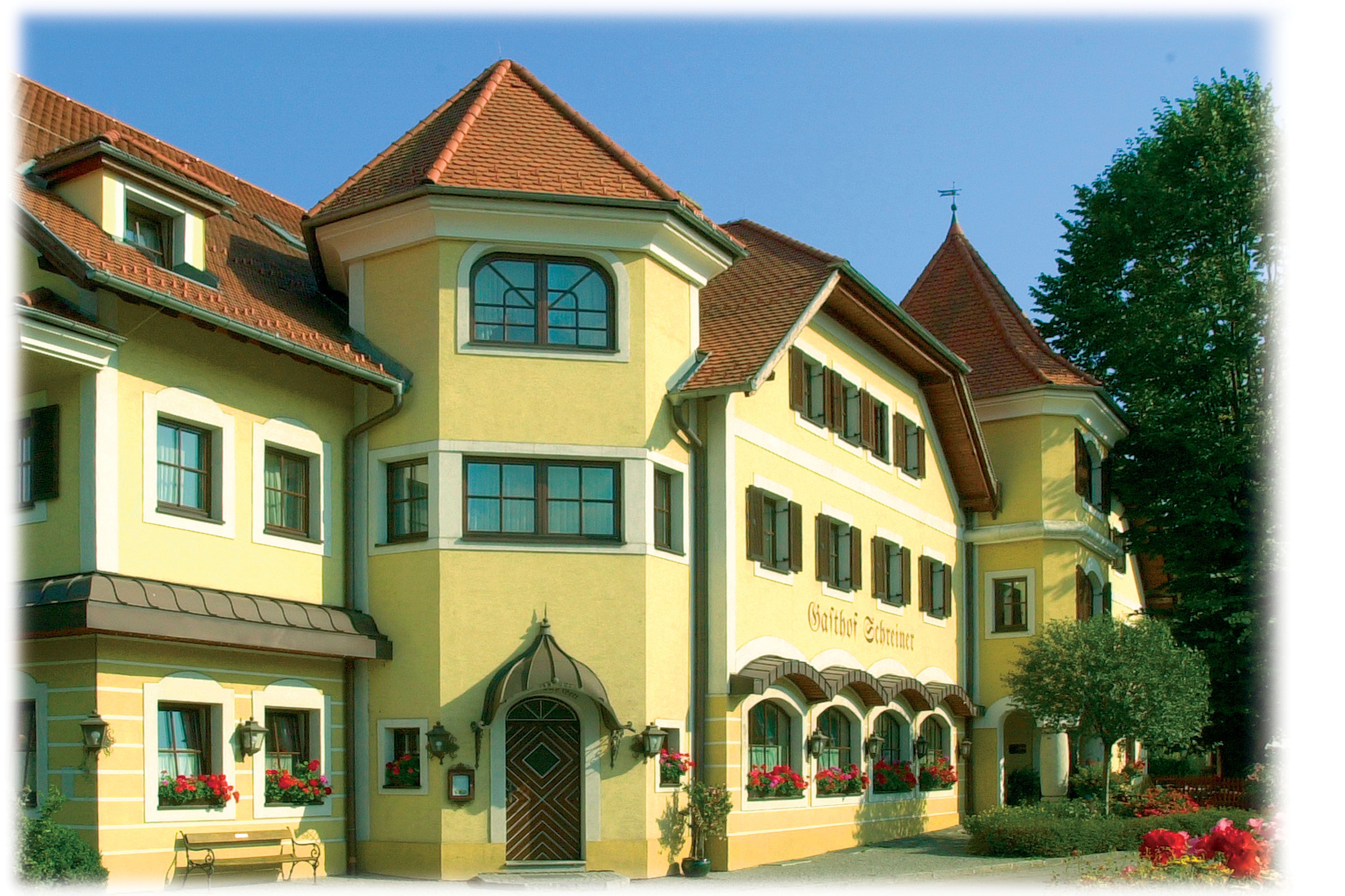 Gelbes Gebäude mit roten Dächern und vielen Fenstern, umgeben von Bäumen.