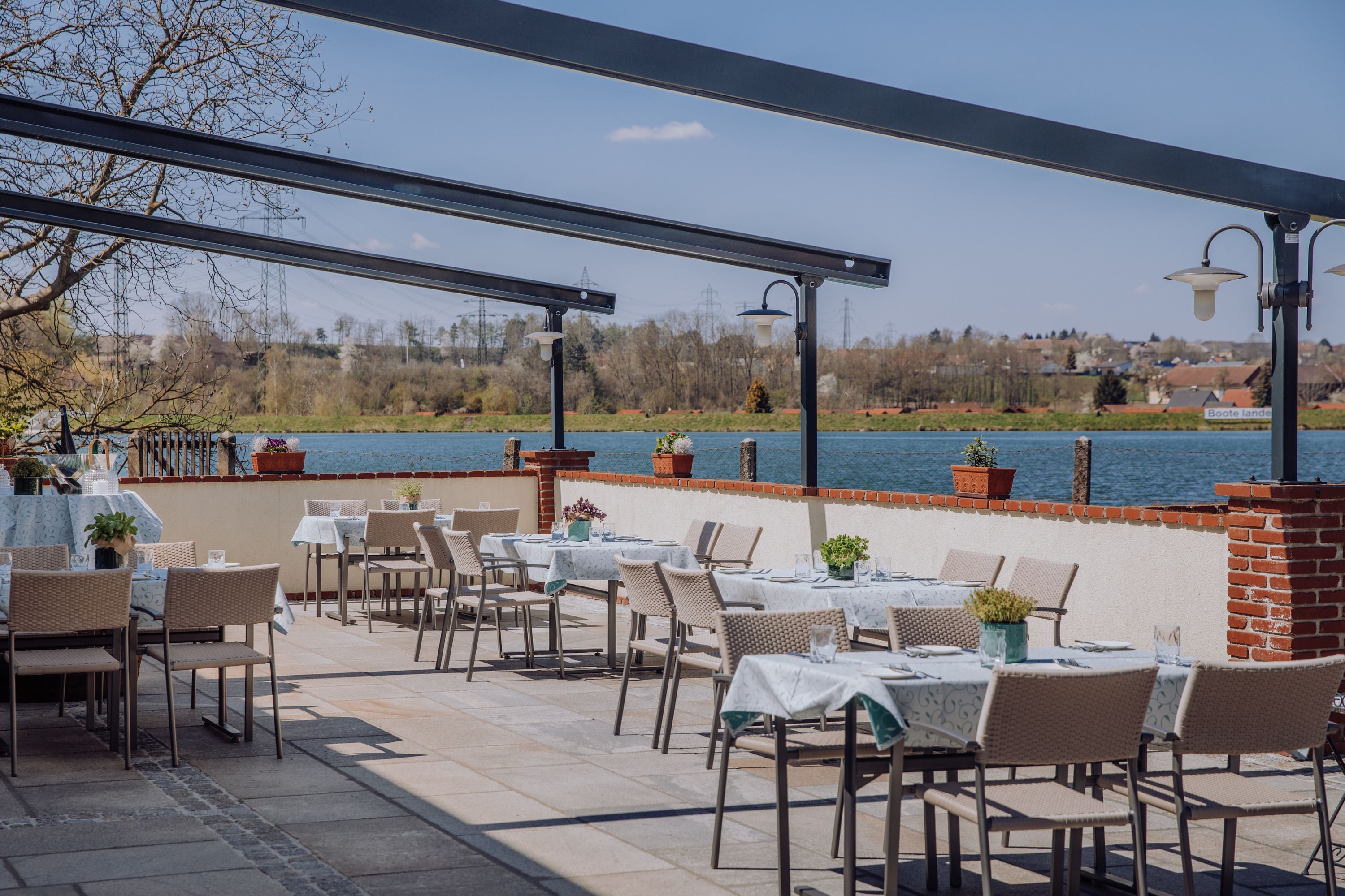 Terrasse mit Tischen und Stühlen, Blick auf einen Stausee und umliegende Landschaft.
