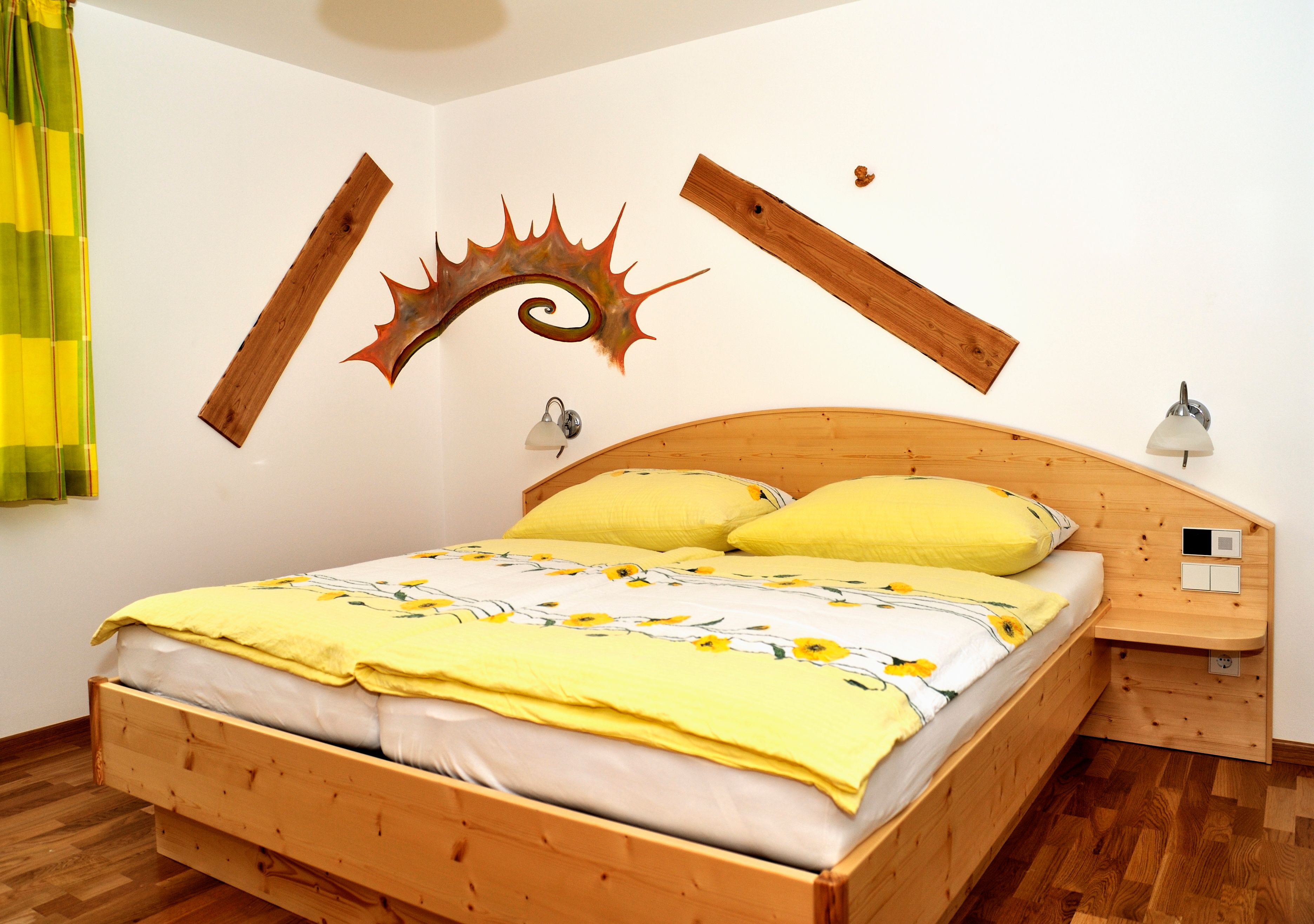 Ein gemütliches Schlafzimmer mit einem Holzbett, gelber Bettwäsche und dekorativen Holzelementen an der Wand.
