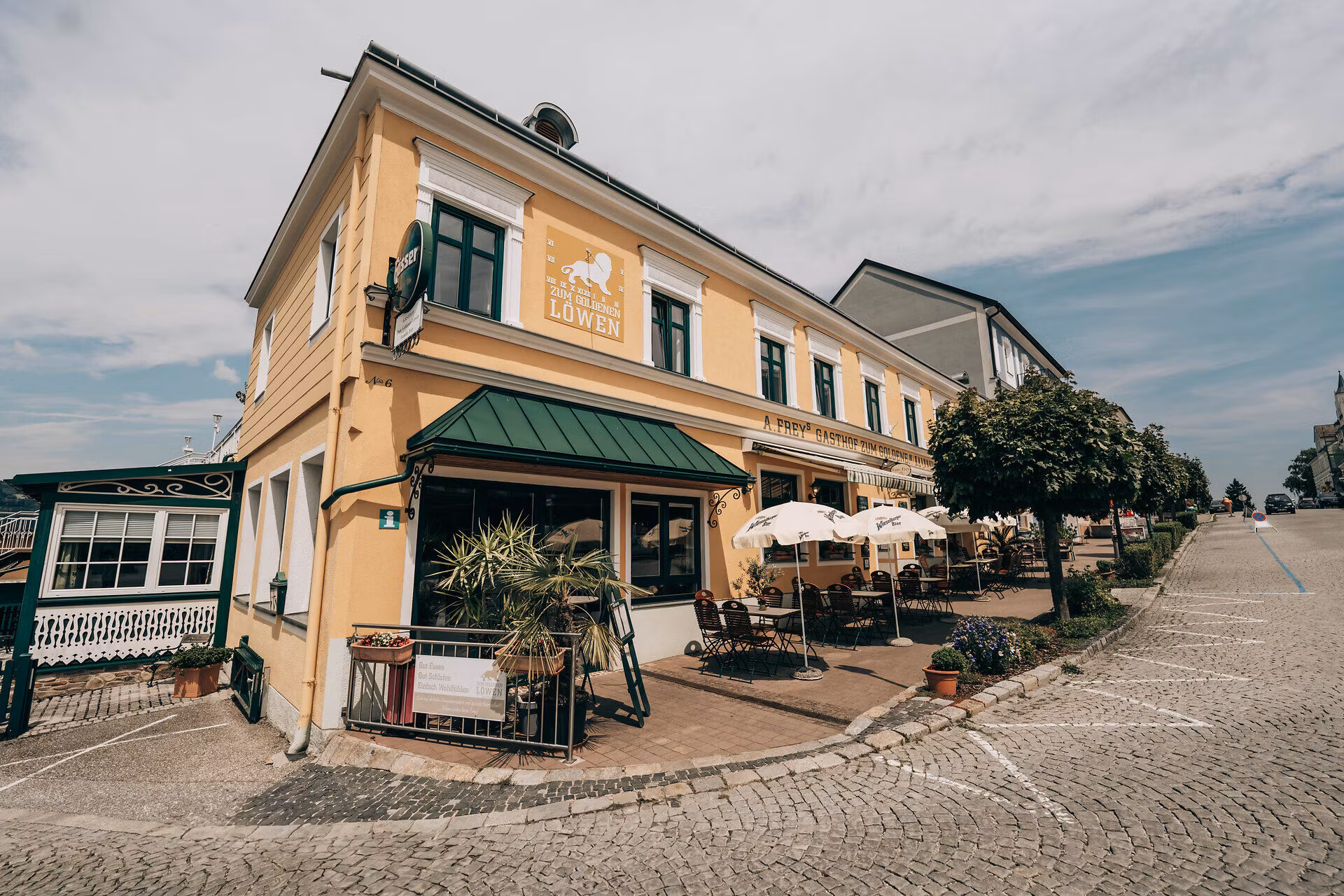 Außenansicht eines gelben Gasthauses mit Terrasse und Sonnenschirmen.