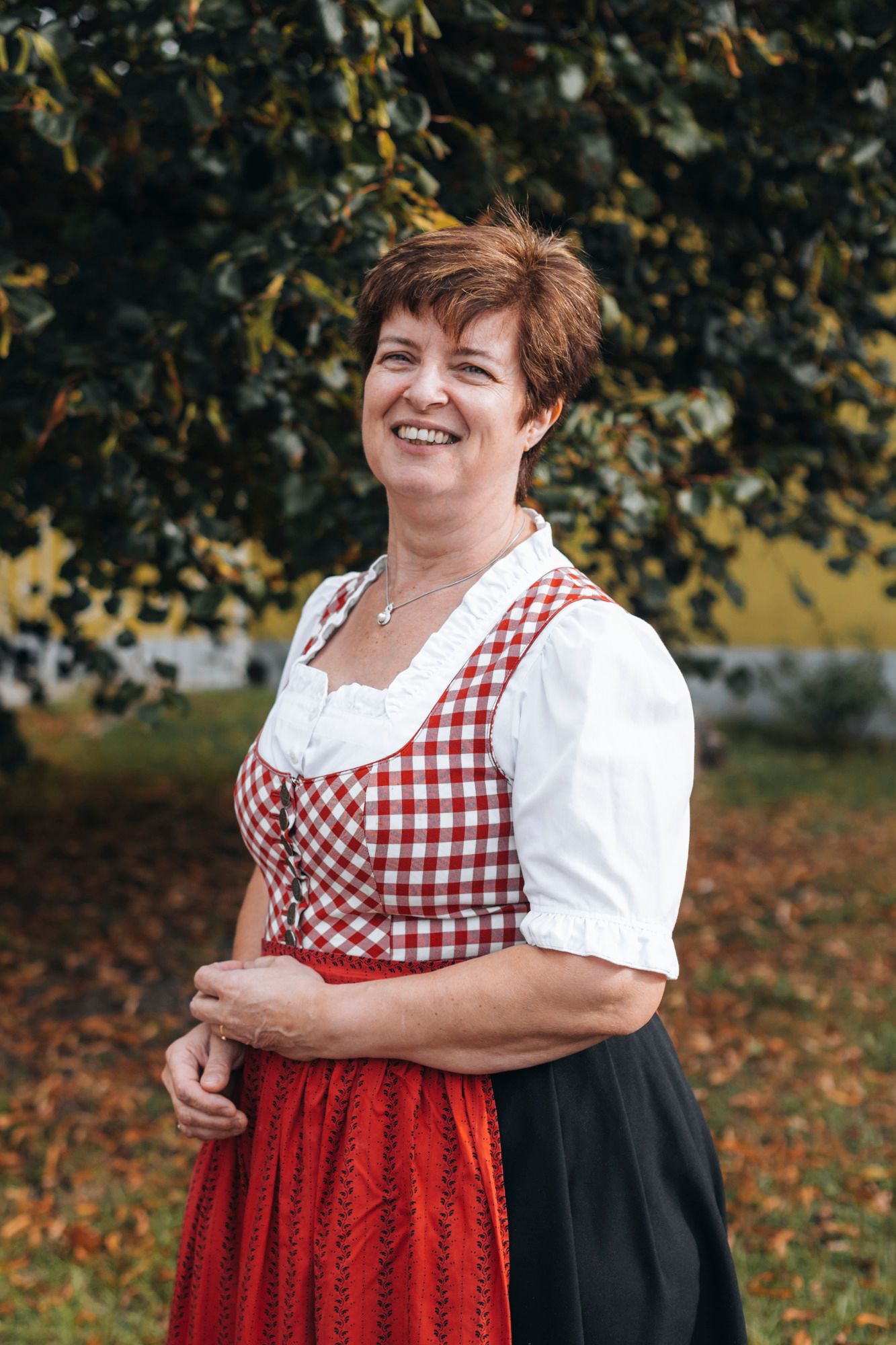 Woman in traditional costume in front of a tree outdoors.
