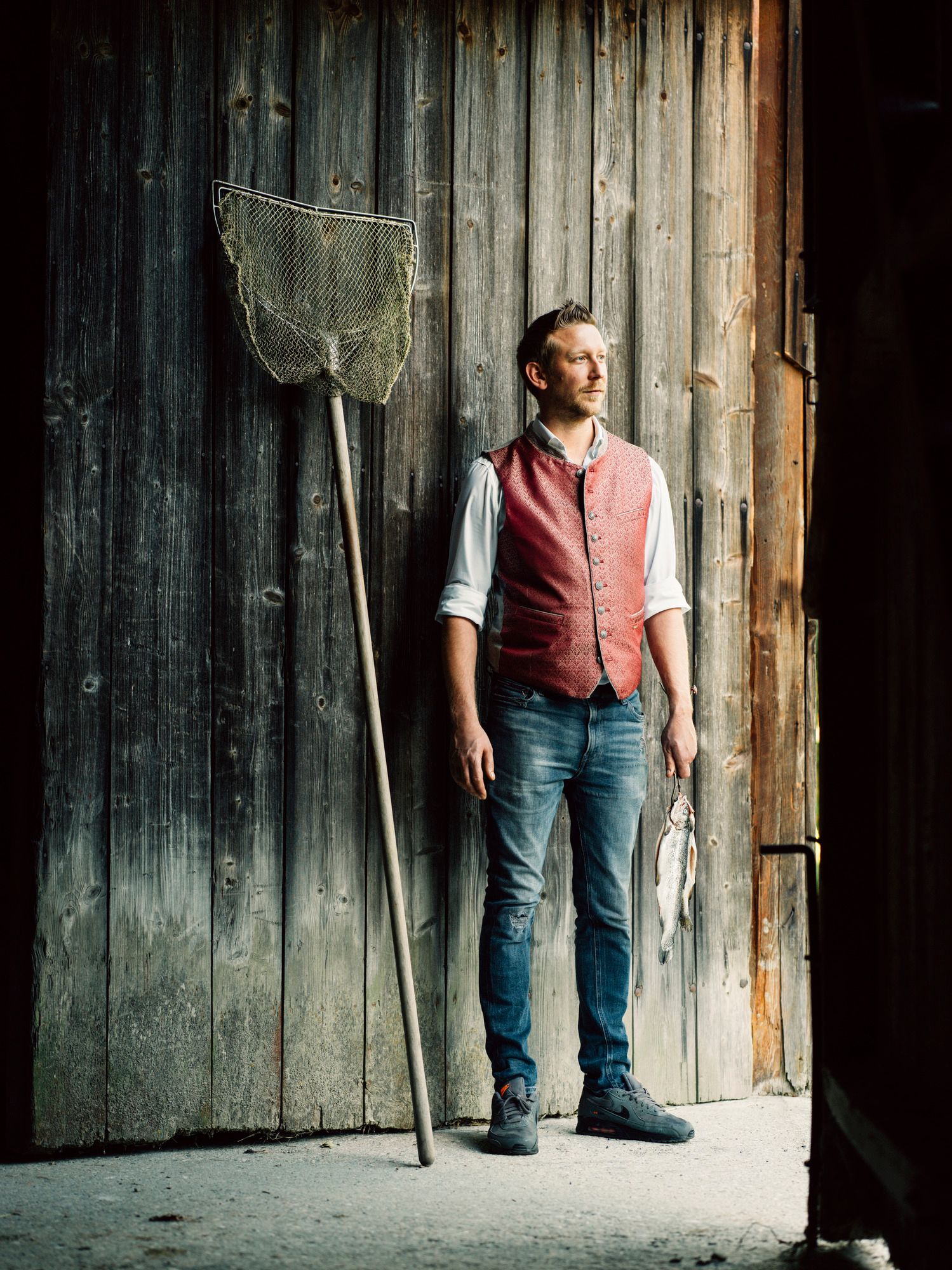 Ein Mann in traditioneller Kleidung steht neben einem Fischernetz und hält einen Fisch in der Hand.