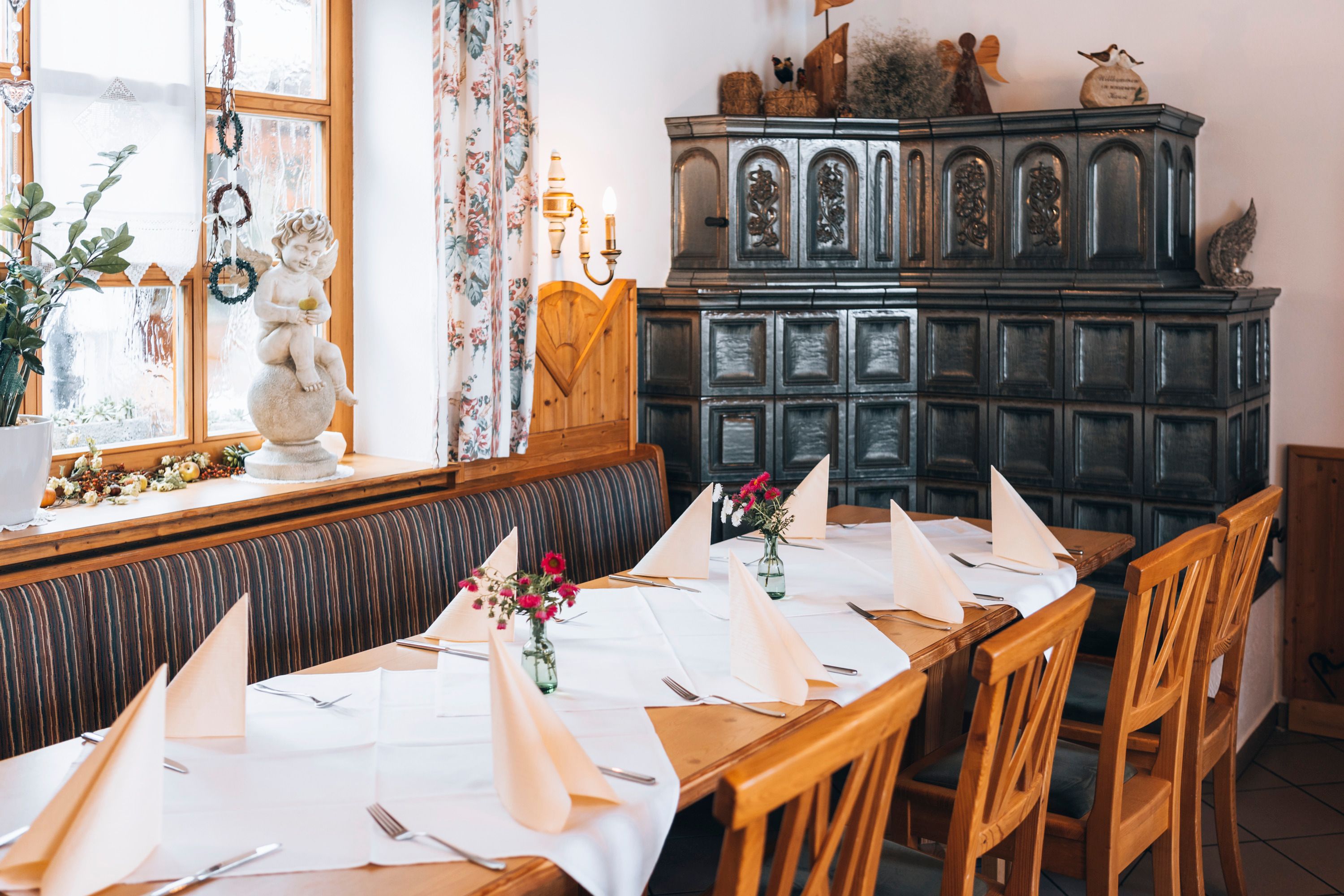 Gemütlicher Essbereich mit Holzmöbeln, Kachelofen und Tischdekoration.