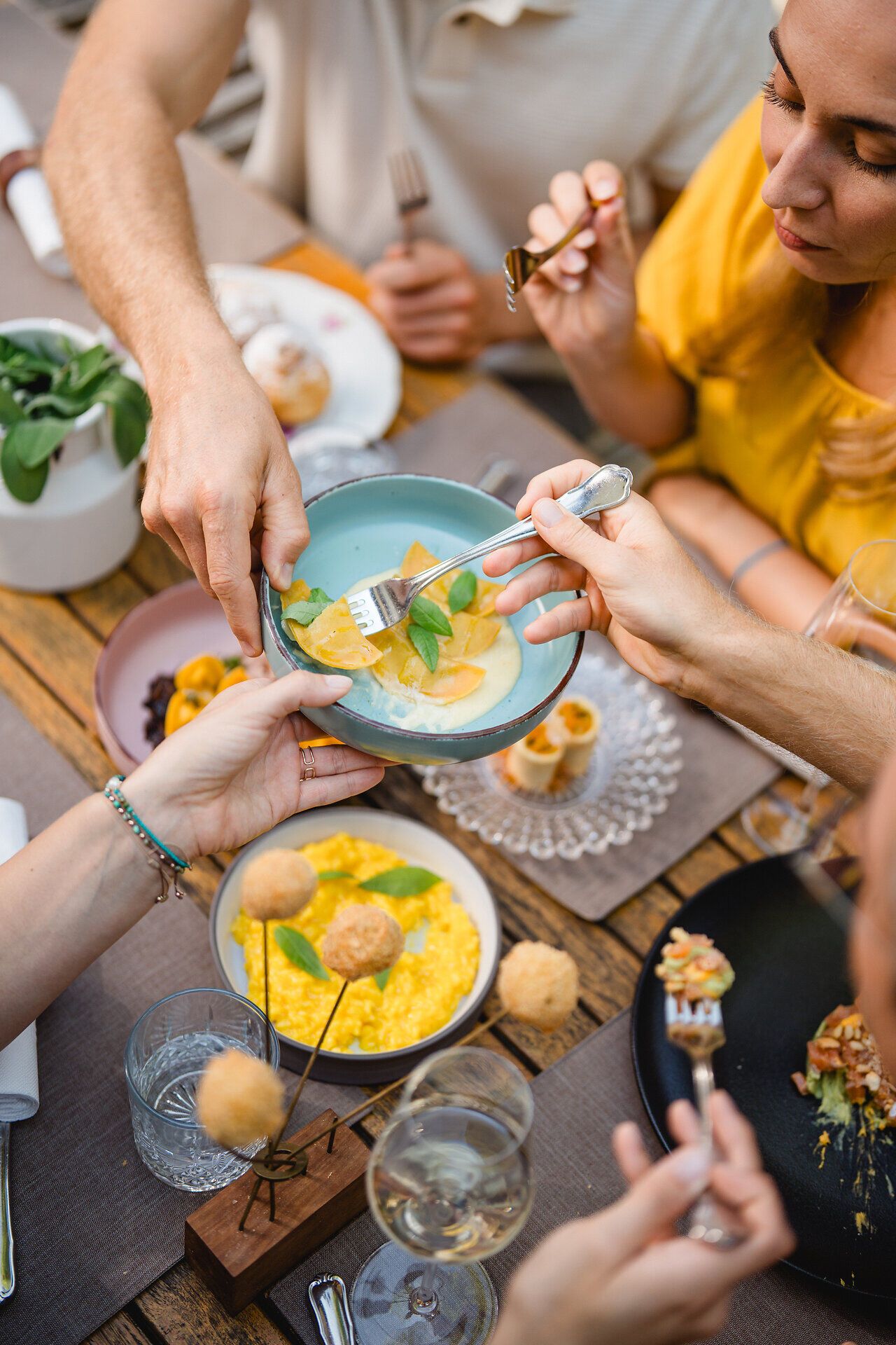 Eine Gruppe von Gästen teilt diverse Gerichte am Tisch im Gastgarten im Wirtshaus Beringer in Mank, darunter gefüllte selbstgemachte Pasta, Knödel und andere kleine Häppchen zum Teilen. 
