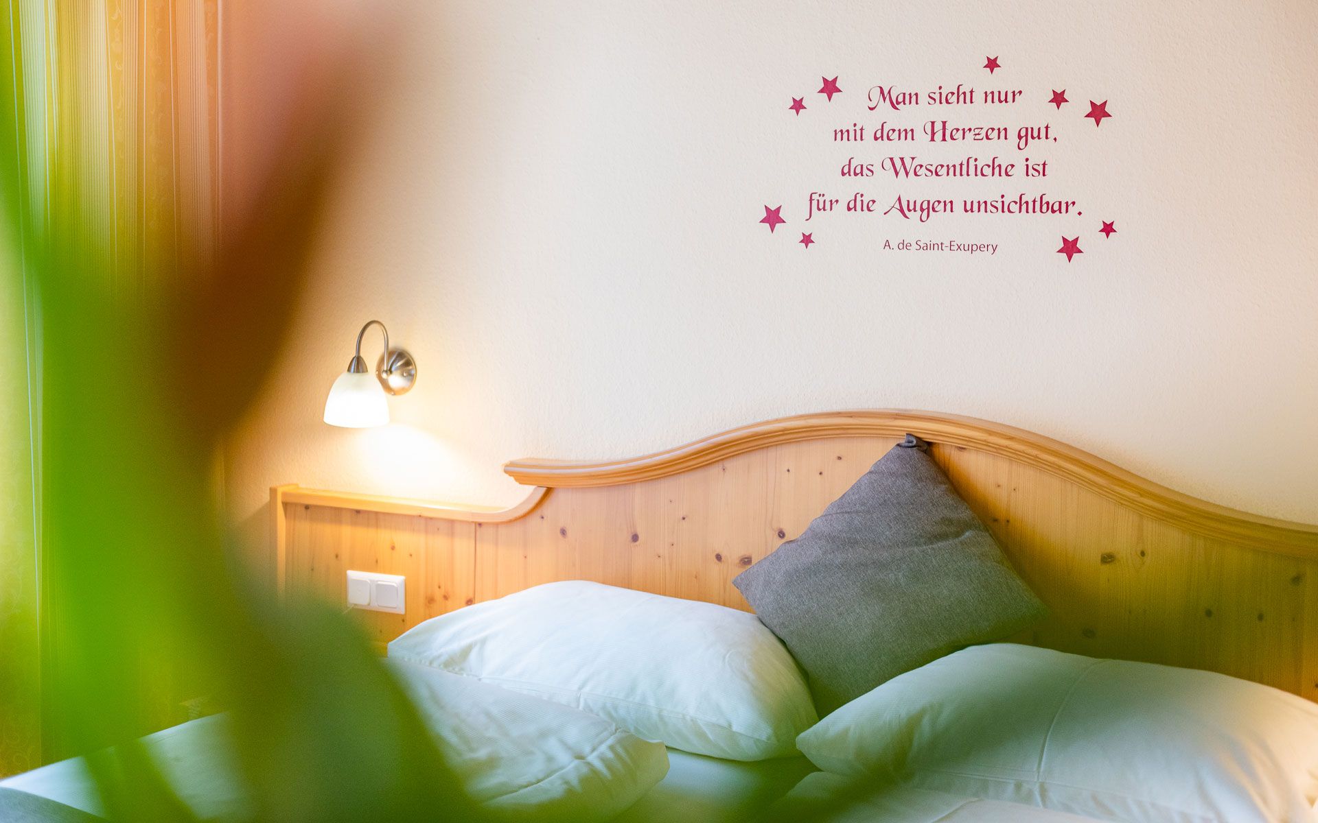 Gemütliches Schlafzimmer mit Zitat an der Wand und Holzkopfteil.