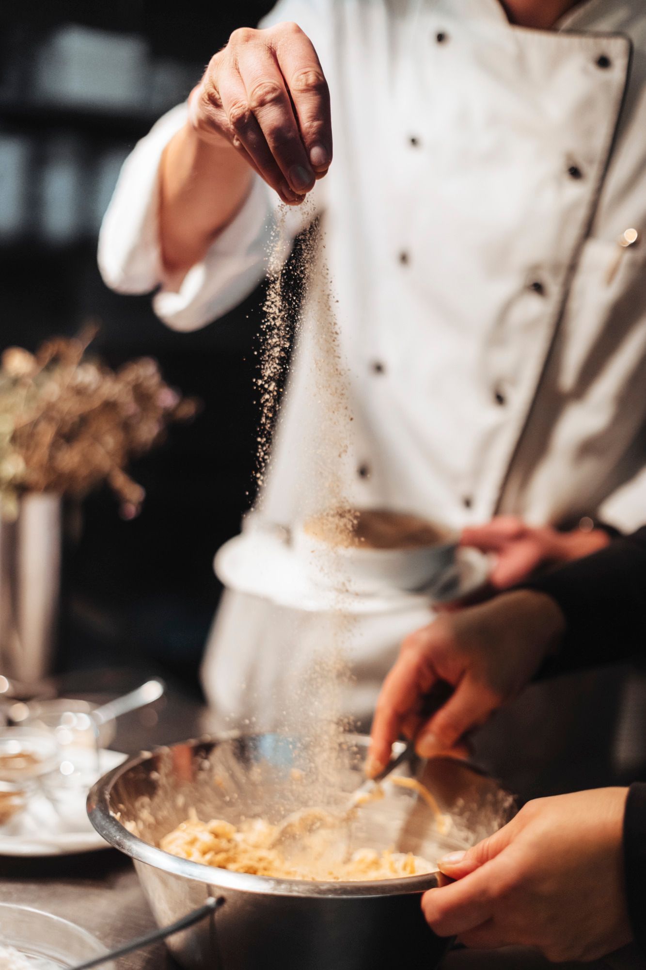 Ein Koch in weißer Uniform streut Gewürze in eine Schüssel mit Teig.