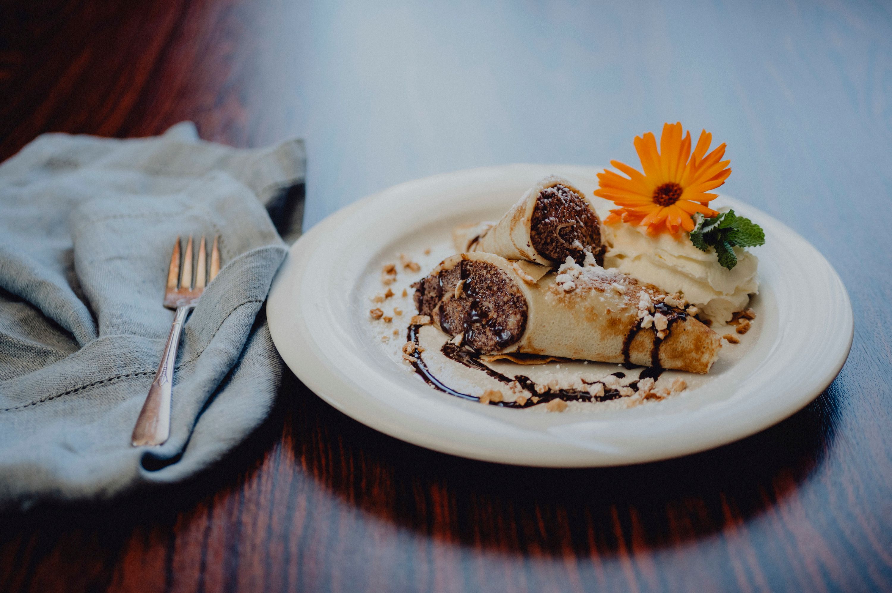 Dessert plate with filled pancakes, cream, chocolate sauce and flower.
