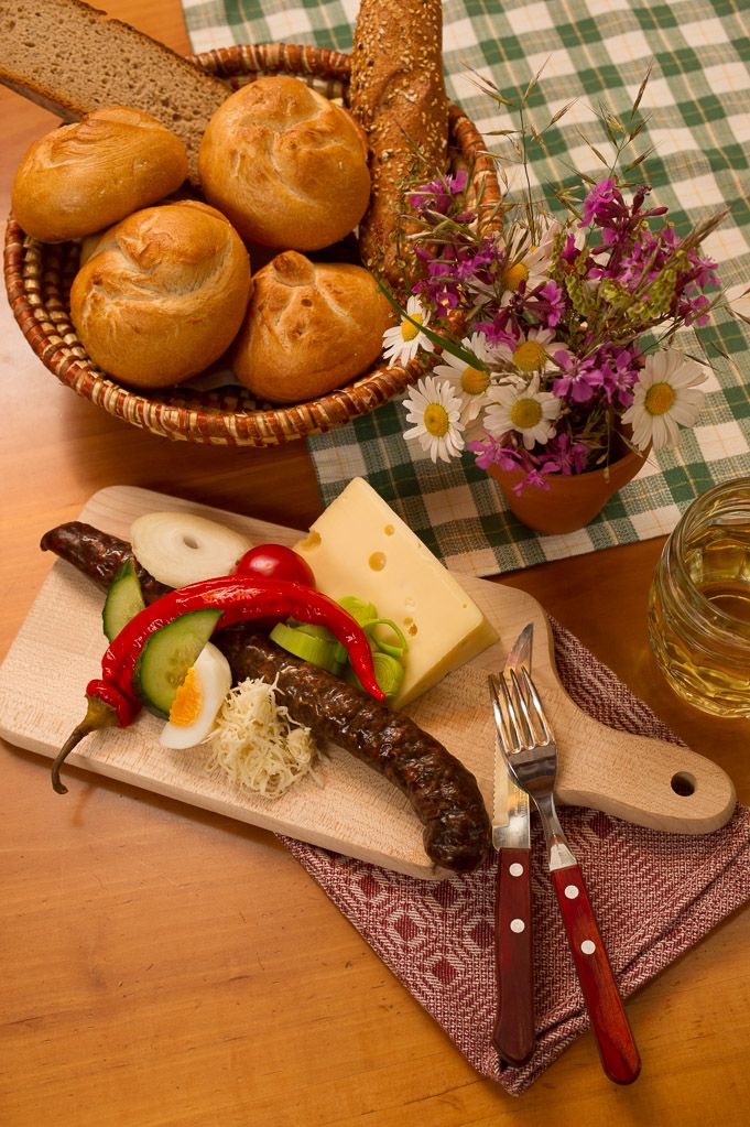 Ein traditionelles Jausenbrett mit Wurst, Käse, Gemüse und Brot auf einem Holztisch.