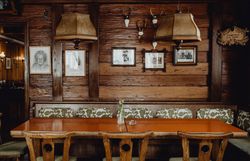 In einem gemütlichen Wirtshaus, umgeben von warmem Holz und nostalgischen Bildern, lädt der große Tisch zu geselligen Runden ein. Die sanfte Beleuchtung der Lampen schafft eine einladende Atmosphäre, perfekt für entspannte Abende mit Freunden und Familie.