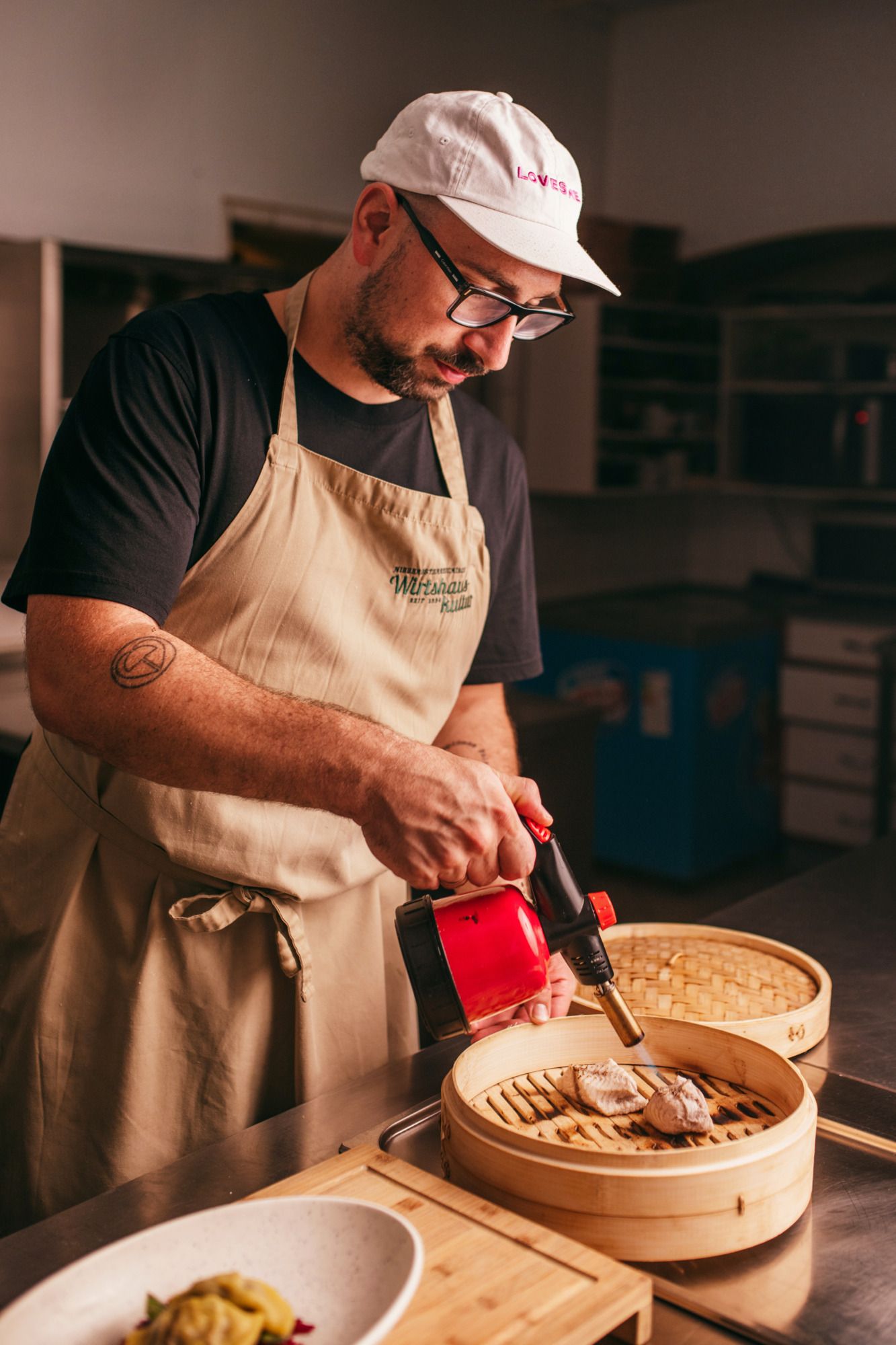 Ein Mann mit Schürze und Mütze flambiert Fisch in einem Bambusdämpfer.