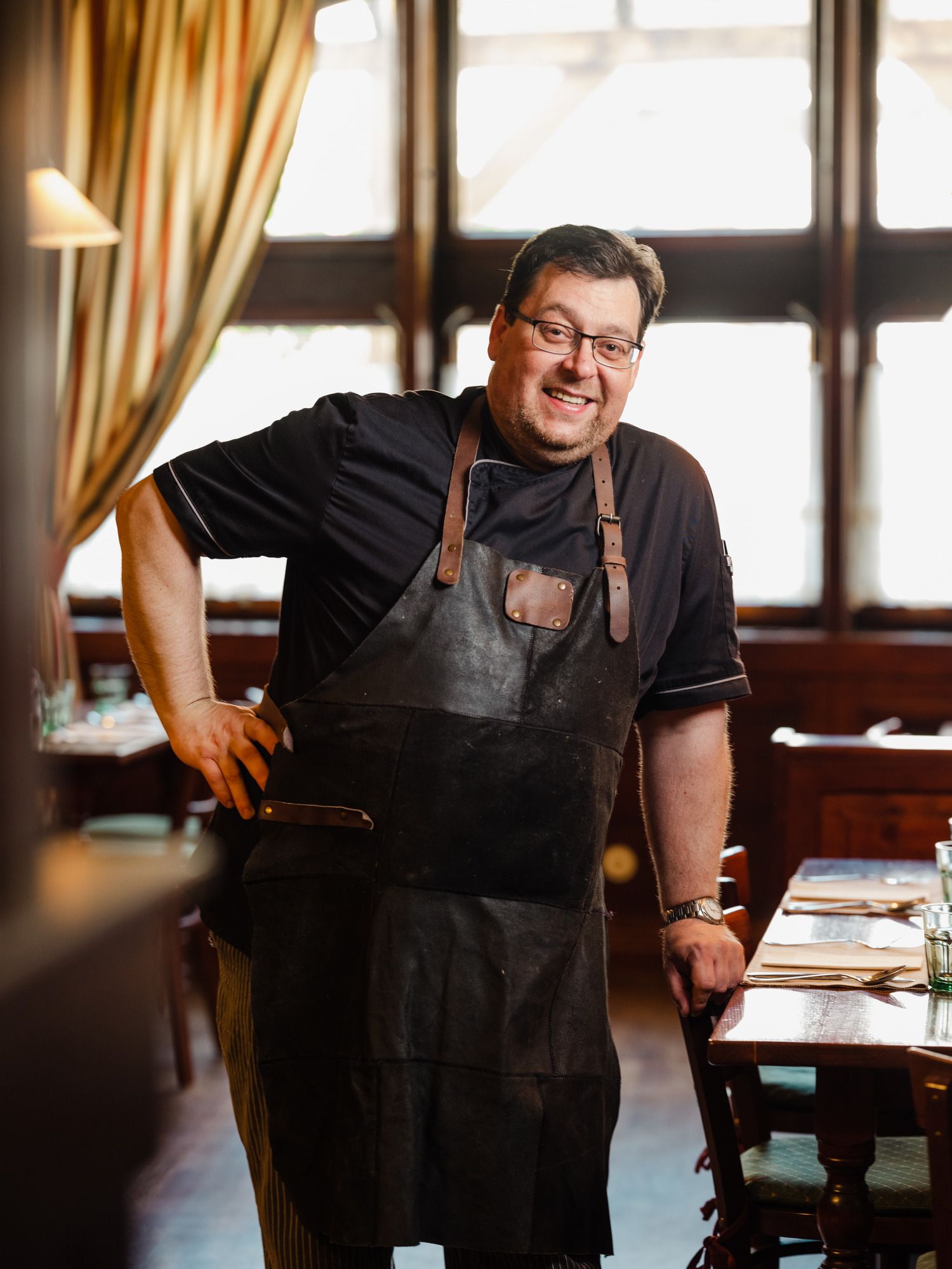 Mann in schwarzer Schürze lächelt in einem gemütlichen Restaurant.