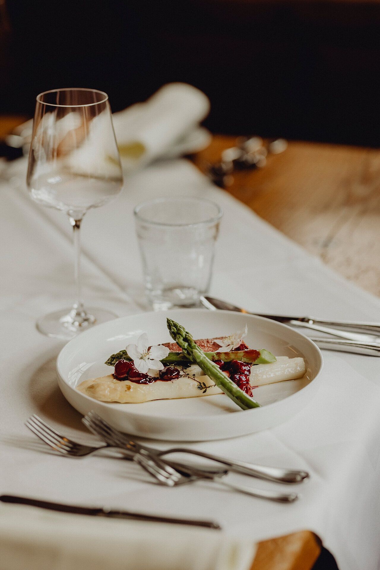 Ein kunstvoll angerichteter Teller präsentiert zarten Rehrücken, umgeben von frischem Spargel und verführerischen Lavendelkirschen. Die harmonische Komposition aus Farben und Aromen lädt dazu ein, die kulinarischen Köstlichkeiten der Region zu entdecken und zu genießen.