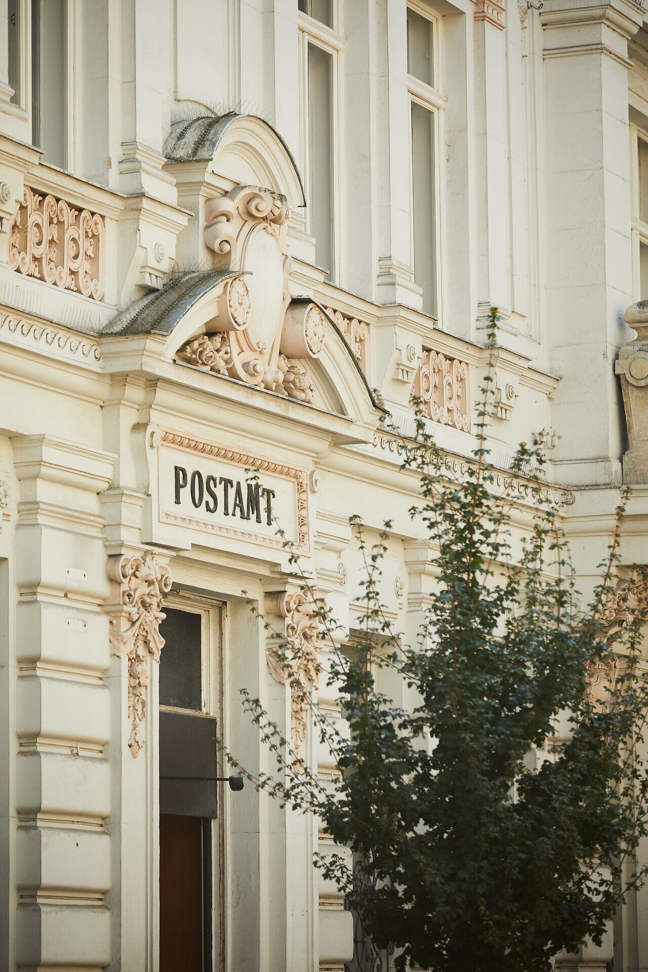 Die prächtige Fassade des Postamts strahlt historische Eleganz aus und lädt Passanten ein, einen Moment innezuhalten. Umgeben von sanften Bäumen und dem pulsierenden Leben der Innenstadt, vermittelt dieser Ort ein Gefühl von Gemeinschaft und Tradition. Hier trifft modernes Stadtleben auf charmante Architektur, die Geschichten aus vergangenen Zeiten erzählt.