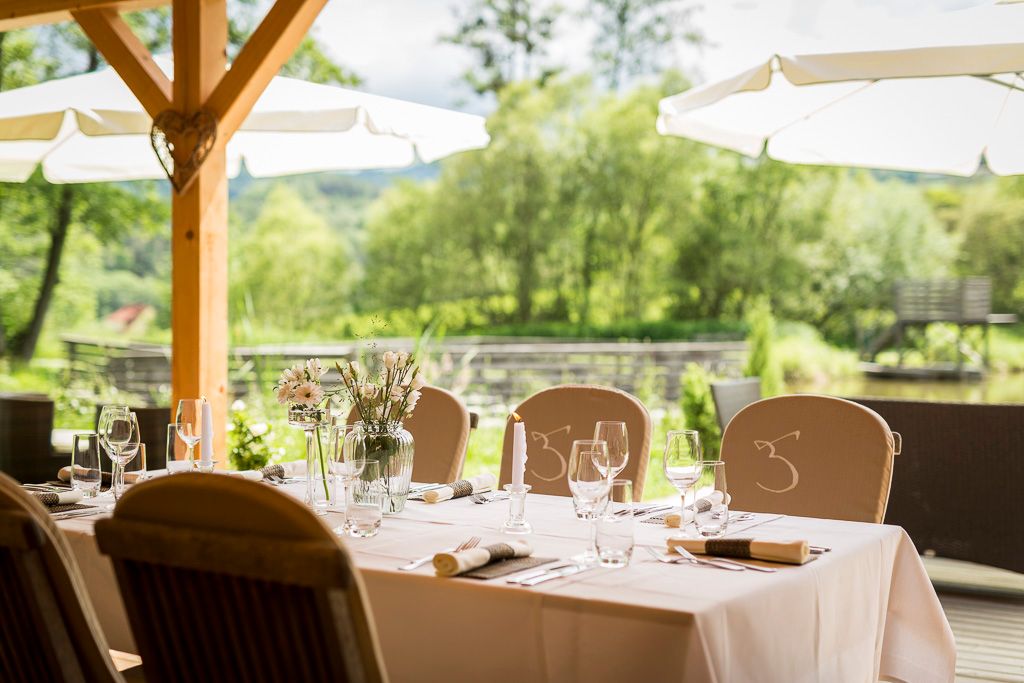 Gedeckter Tisch im Freien mit Blick auf einen Teich und Bäume.