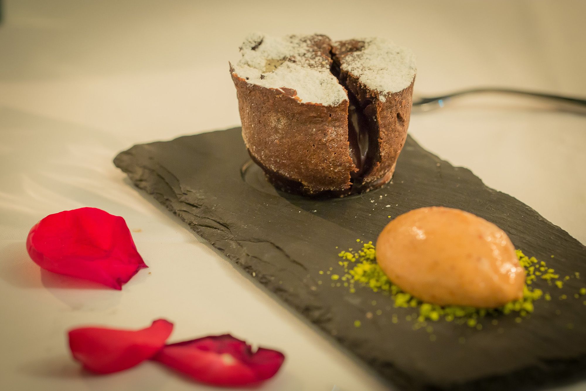 Ein Schokovulkan-Dessert auf einer Schieferplatte mit einer Kugel Eis und roten Rosenblättern.